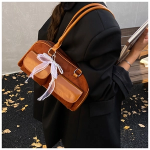 Detail of caramel suede hobo bag with lace bow and pearl charms worn over the shoulder