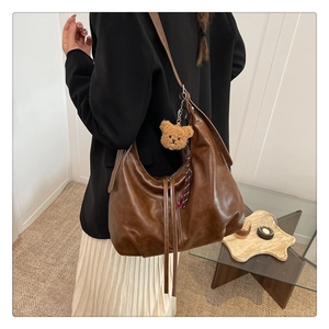 Détail d'un grand sac hobo en cuir marron porté par un mannequin dans un décor chaleureux