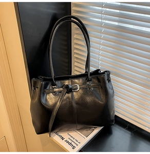 Détail d'un sac cabas en cuir noir brillant avec boucle métallique sur fond artistique