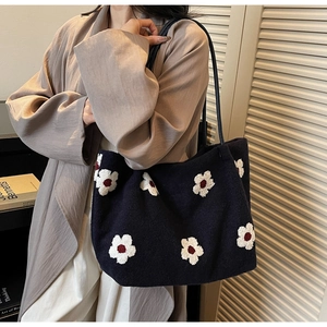 Detail of floral embroidery on a dark fabric tote bag with slim leather straps