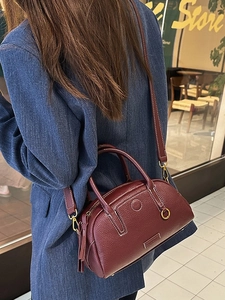 Deep wine red pebbled leather bowling bag with gold hardware worn by a model