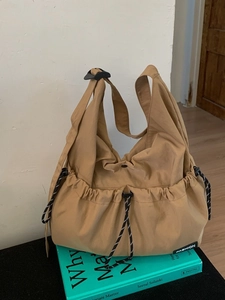 Large khaki nylon crossbody bag with drawstring pocket on green books background