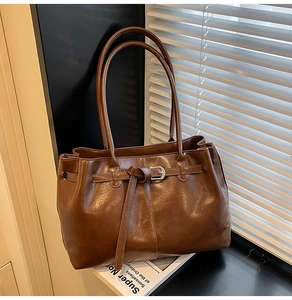 Détail du sac cabas en cuir brillant marron foncé avec boucle argentée et nœud décoratif