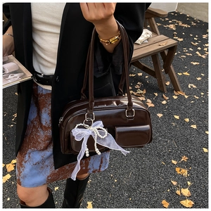 Detail of dark brown patent leather shoulder bag with lace bow and pearl pendant
