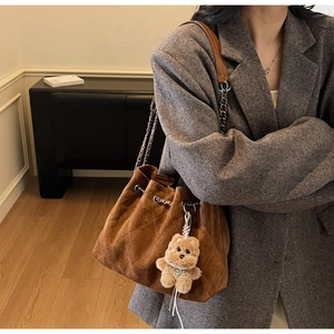 Close-up of brown quilted suede bucket bag with chain strap and plush bear charm detail