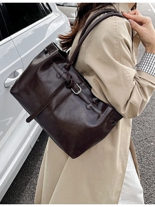 Grand sac cabas rétro en cuir marron foncé avec boucle latérale porté avec un trench