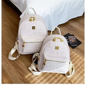 Dettaglio di zaini in tweed beige e rosa con finiture in metallo dorato su parquet