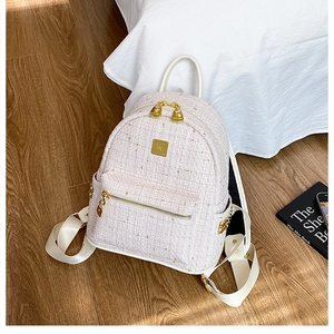 Dettaglio dello zaino in tweed beige con finiture dorate e logo su superficie in legno