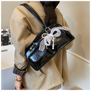 Detail of black patent leather shoulder bag with white mesh bow and pearl decorations
