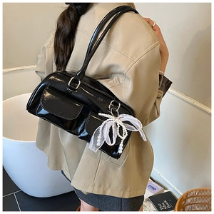 Detail of black glossy shoulder bag featuring pearl charms and a delicate white bow accent