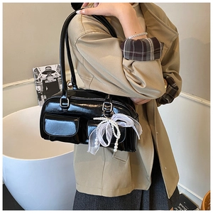 Close-up of black patent leather shoulder bag with pearl chain and lace bow charm detail