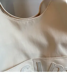 Vue détaillée de la texture du cuir synthétique beige avec broderie de lettres soignée