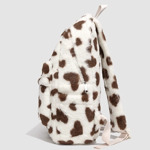 Close-up of cow print plush backpack featuring side pockets and silver metal zippers