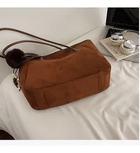 Gros plan sur un cabas en daim marron avec breloque en peluche, perles en bois et logo embossé
