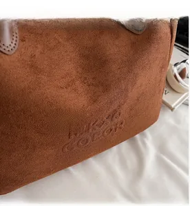 Gros plan du sac cabas marron en daim montrant le logo embossé et les détails de couture