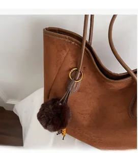 Détail du sac cabas en daim marron avec breloque boule peluche et logo embossé
