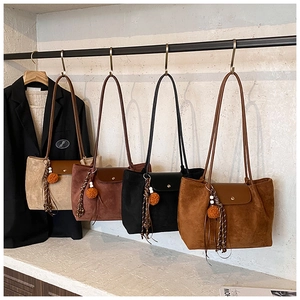 Detail view of large suede tote bags in four colors with decorative tassels on hangers