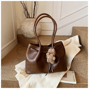 Detail of a dark brown faux leather tote bag with a cute plush bear charm on soft steps