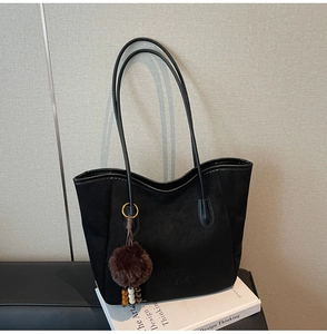Détail du sac cabas en daim noir avec lanières en cuir et breloque pompon en peluche