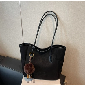 Détail d'un cabas en daim noir avec bretelles en cuir et pompon décoratif en peluche