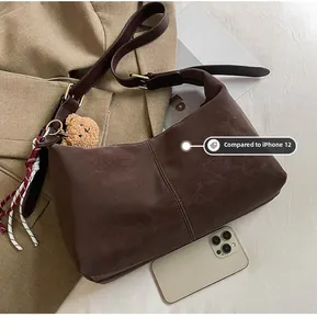 Brown leather dumpling bag detail with plush bear charm and phone for size reference