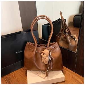 Detailed close-up of brown leather tote bag with drawstring and plush bear charm