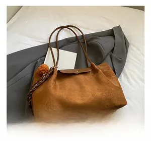 Detail of brown suede tote bag with metal magnetic closure and plush pompom tassel charm