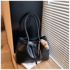 Detail of vintage black PU tote bag texture with buckles and bear charm on wood surface