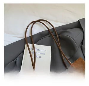 Detail of brown suede tote bag with smooth leather flap and pompom charm on a blazer