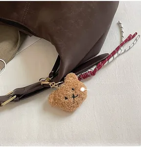 Detail of dark brown dumpling bag with a cute plush bear pendant and woven red strap