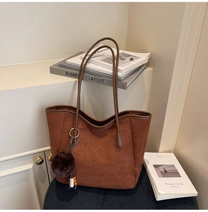 Détail d'un sac cabas en daim marron foncé avec un pompon en peluche et perles chic