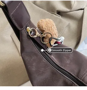 Detail view of the smooth golden zipper and plush bear charm on the dark brown crossbody bag
