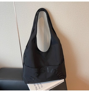 Gros plan du sac cabas noir en toile avec logo 3D en relief et large bandoulière souple