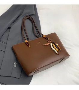 Close-up of brown leather tote bag with colorful wood bead charm on gray suit