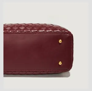 Dettaglio della borsa a secchiello bordeaux in pelle intrecciata con borchie dorate