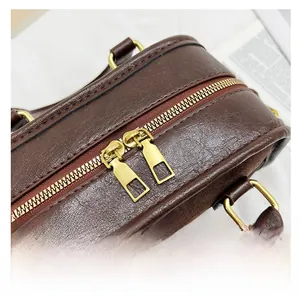 Vue macro de la double fermeture éclair dorée sur sac Boston en cuir grainé marron foncé