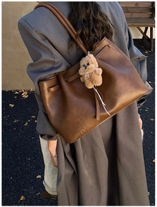 Detail of dark brown leather tote bag with plush dog charm against autumn street background