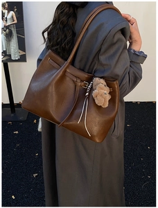 Detail of deep brown leather tote bag with decorative bear pendant and stylish metal buckle