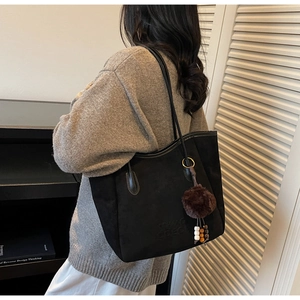 Détail du sac cabas noir en daim avec charm en peluche et logo sur un cardigan gris