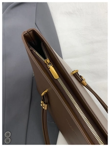 Close-up of golden zipper detail and metal rivets on a vintage brown leather tote bag