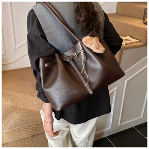Close-up of a large dark brown tote bag with leather texture and cute plush pendant
