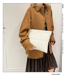 Detailed close-up of a white quilted padded clutch bag held by a model in brown outfit