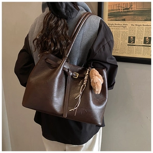 Close-up of a vintage brown leather tote bag with stylish buckle and plush charm detail