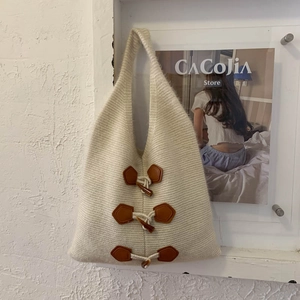 Close-up of cream knit tote bag showing thick wool texture and decorative horn buckles