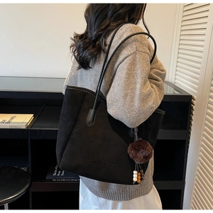 Détail du sac cabas en daim noir avec lanières en cuir et pendentif pompon décoratif