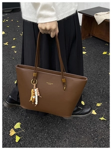 Close-up of brown tote bag with gold logo lettering and decorative wooden bead tassel