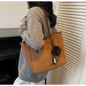 Détail d'un sac cabas en daim avec logo MKY COE et breloque pompon en peluche marron