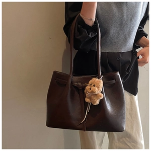 Close-up of brown matte leather tote bag featuring a plush bear charm with pearls