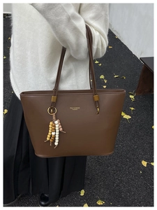 Detail of a brown leather tote bag with gold lettering and decorative beaded tassel