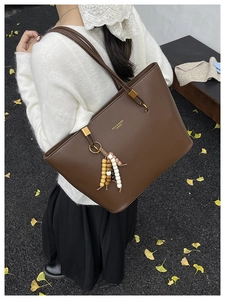 Detail of dark brown tote bag with beaded tassel and metallic logo on outdoor background